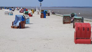 A beach with numbered beach huts and a large blue sign. - Cozy apartment - incl. Beach chair Apr-Sep, small and quiet residential complex (Dornumersiel)