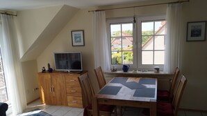 A dining area with a wooden table and chairs, a television on a wooden cabinet, and a window with curtains. - Cozy apartment - incl. Beach chair Apr-Sep, small and quiet residential complex (Dornumersiel)