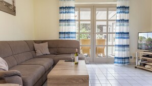Una sala de estar con un sofá marrón, una mesa de centro de madera, un televisor sobre un mueble bajo y una ventana con cortinas a rayas azules.
