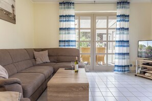 Un soggiorno con un divano marrone, un tavolino in legno, una TV su un mobile e una finestra con tende a righe blu.