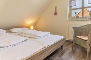 Una camera da letto con due letti, un comodino con una lampada, una sedia in vimini e una finestra con vista su un edificio.