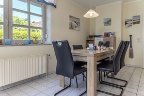 Un espace repas avec une table en bois, des chaises noires, un luminaire suspendu et une vue sur la verdure à l’extérieur.