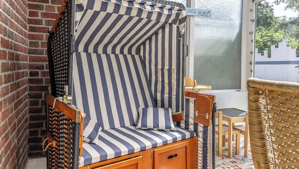 Una silla a rayas con un mueble de madera, una silla de mimbre y un letrero que dice 'LINGS PLATZ'.