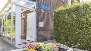 Una entrada de edificio con puerta de vidrio, un cartel azul en la calle y una maceta con flores.