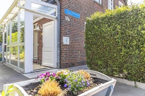 L'ingresso di un edificio con una porta in vetro, una targa stradale blu e un aiuola.