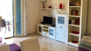 Un salon moderne avec un téléviseur, un meuble de rangement blanc et une bibliothèque.