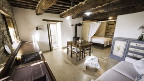 A cozy room with a wooden ceiling, a bed with white curtains, a dining table with chairs, and a kitchenette with a stove. - Appartamentino Rustico in Villa Maindi with garden use and free WiFi (Pennabilli)