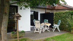 A patio with a table and chairs, a birdhouse, and a hedge. - Luxury holiday home, 100 meters from forest, swimming pool nearby, 4 km from Edersee (Frankenau)