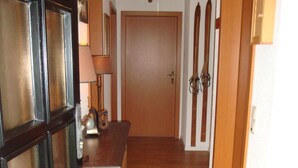 A hallway with a wooden floor, a door with glass panels, a wooden table with a lamp, and a door with a coat rack. - Luxury holiday home, 100 meters from forest, swimming pool nearby, 4 km from Edersee (Frankenau)