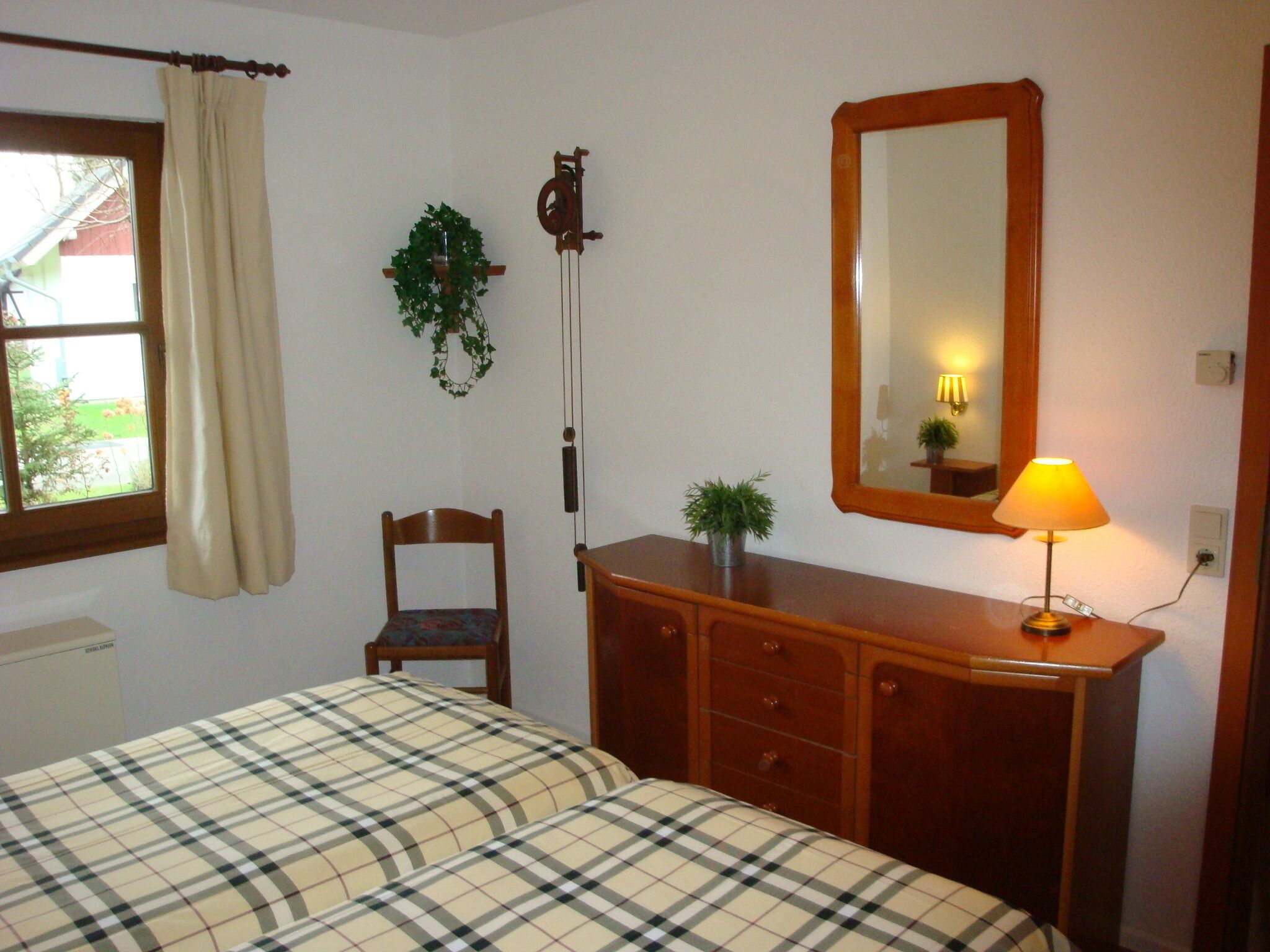 A bedroom with a bed, a wooden dresser, a chair, a mirror, and a window with curtains.
