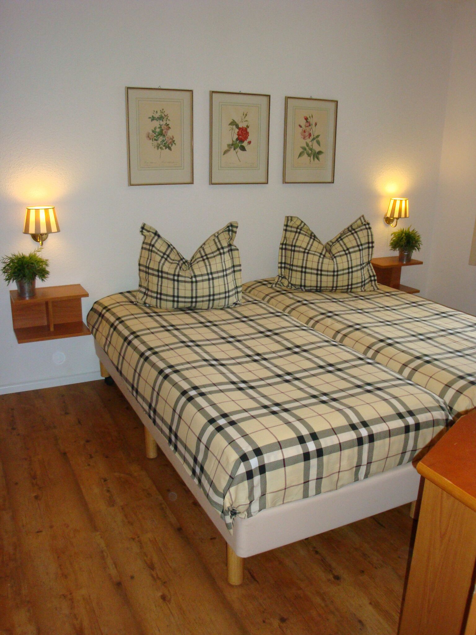 Ein Schlafzimmer mit einem Doppelbett, zwei Nachttischen mit Lampen und drei gerahmten floralen Bildern an der Wand.