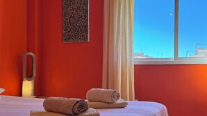 Habitación de hotel con dos camas, una pared roja, una ventana con vistas y un perchero.