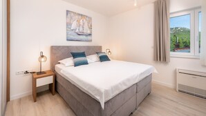 Et soveværelse med seng, sengeborde, lamper, et maleri, et vindue med gardiner og en aircondition.