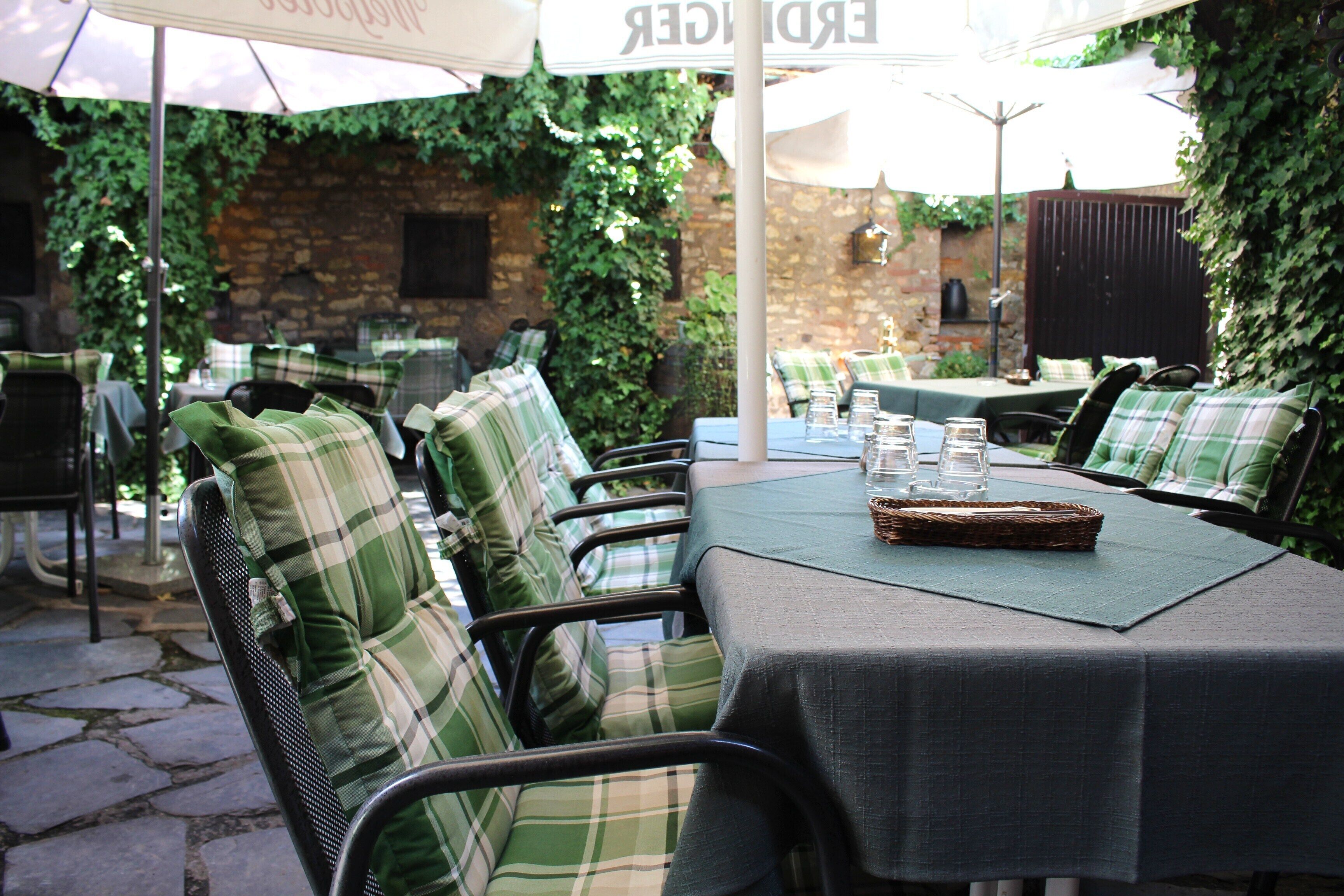 Une terrasse extérieure avec des tables et des chaises, dont certaines sont protégées par des parasols, et un mur de briques orné de verdure.