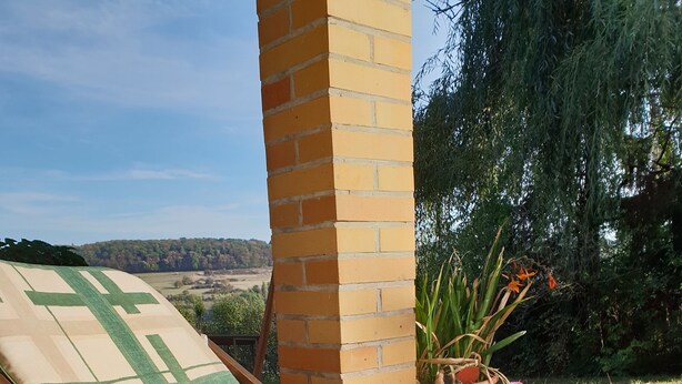 A sun lounger with a cushion, a book, and a potted plant on a patio with a view of the countryside. - Ferienwohnung Peters – 60m² apartment with WiFi, terrace & nature setting (Schotten)