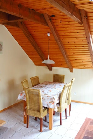A dining area with a wooden ceiling, hexagonal floor tiles, and wicker chairs around a table with a floral tablecloth.
