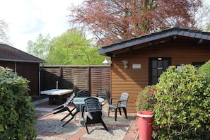 A wooden cabin with a sauna, surrounded by a garden with a table and chairs.