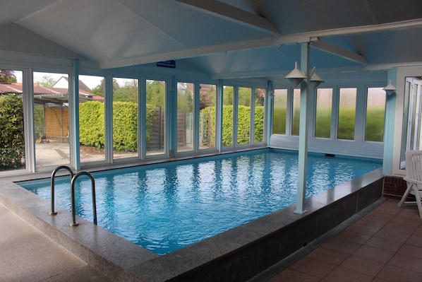 An indoor swimming pool with clear glass walls, a tiled floor, and a metal ladder.