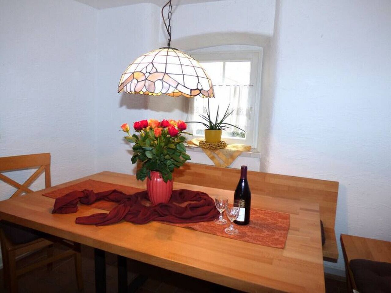 A dining table with a vase of flowers, a bottle of wine, and a red cloth.