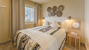 A bedroom with a bed, curtains, a ceiling fan, wall art, and a bedside table with a tissue box. - Sea View Apartment Windsor Park (Adeje)