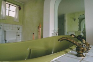 A green bathtub with a vintage faucet, a white tiled wall, and a window with curtains. - Old house to feel good (Usingen)