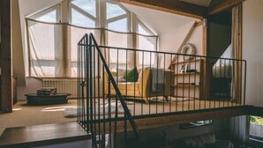 A loft bedroom with a wooden beam ceiling, a black metal railing, a yellow sofa, and a large window. - Old house to feel good (Usingen)