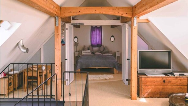 A bedroom with a bed, a TV, and a wooden staircase leading to a lower level. - Old house to feel good (Usingen)