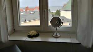 A room with a window overlooking a cityscape, a small table with a decorative item, and a mirror on the window sill.