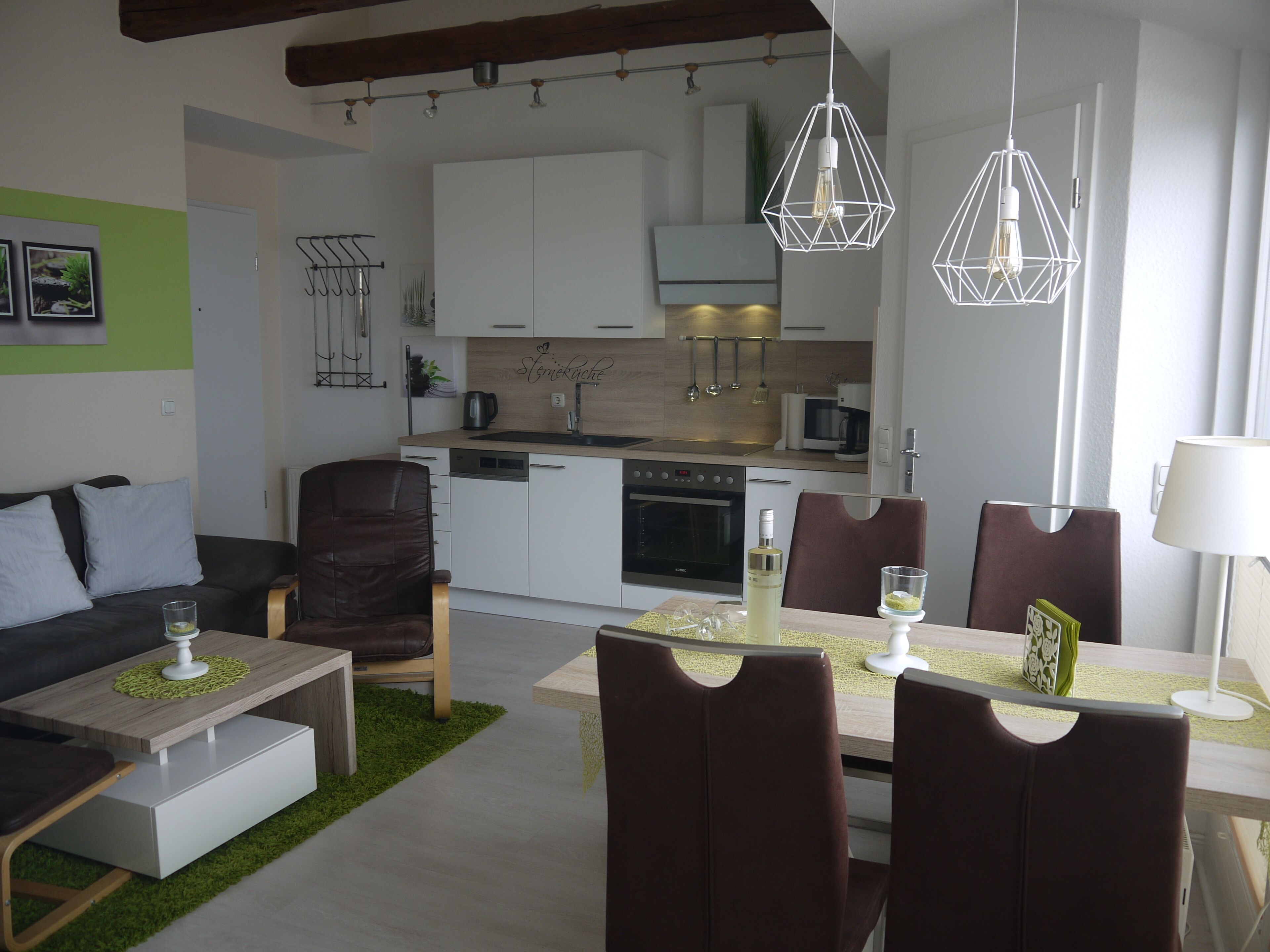 Una cucina moderna con mobili bianchi, un forno a microonde e una lavastoviglie. C'è una zona pranzo con un tavolo apparecchiato per due, una poltrona in pelle marrone e un divano bianco con cuscini.