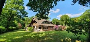 Een huis met schuine dak, schoorsteen en een gazon met een barbecue en stoelen.