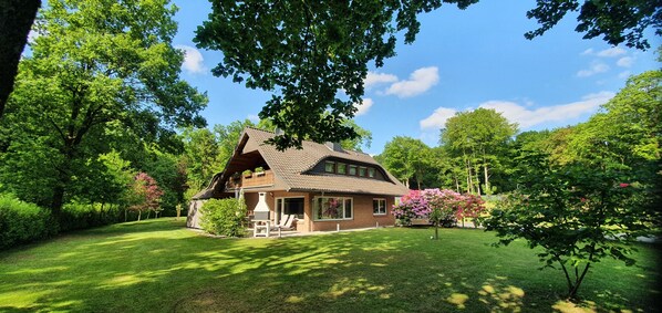 A house with a sloped roof, a chimney, and a lawn with a grill and chairs. - Vacation apartment at Höpen - Lüneburg Heath (Schneverdingen)