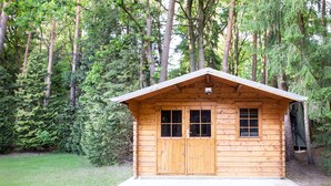 A wooden cabin with a brick entrance, surrounded by dense forest. - Vacation apartment at Höpen - Lüneburg Heath (Schneverdingen)