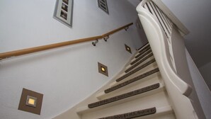 Una escalera con barandilla de madera y pared blanca con tres focos empotrados.