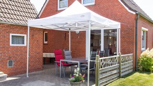 Una casa de ladrillo con un patio, una carpa blanca y mobiliario de exterior.