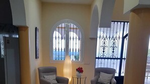 A lobby with two grey armchairs, a small round table with a vase of red flowers, and a large arched window with a view of the sea. - Exclusive CHALET near SEVILLA Andalusia with pool for 14 people  (Lora del Río)