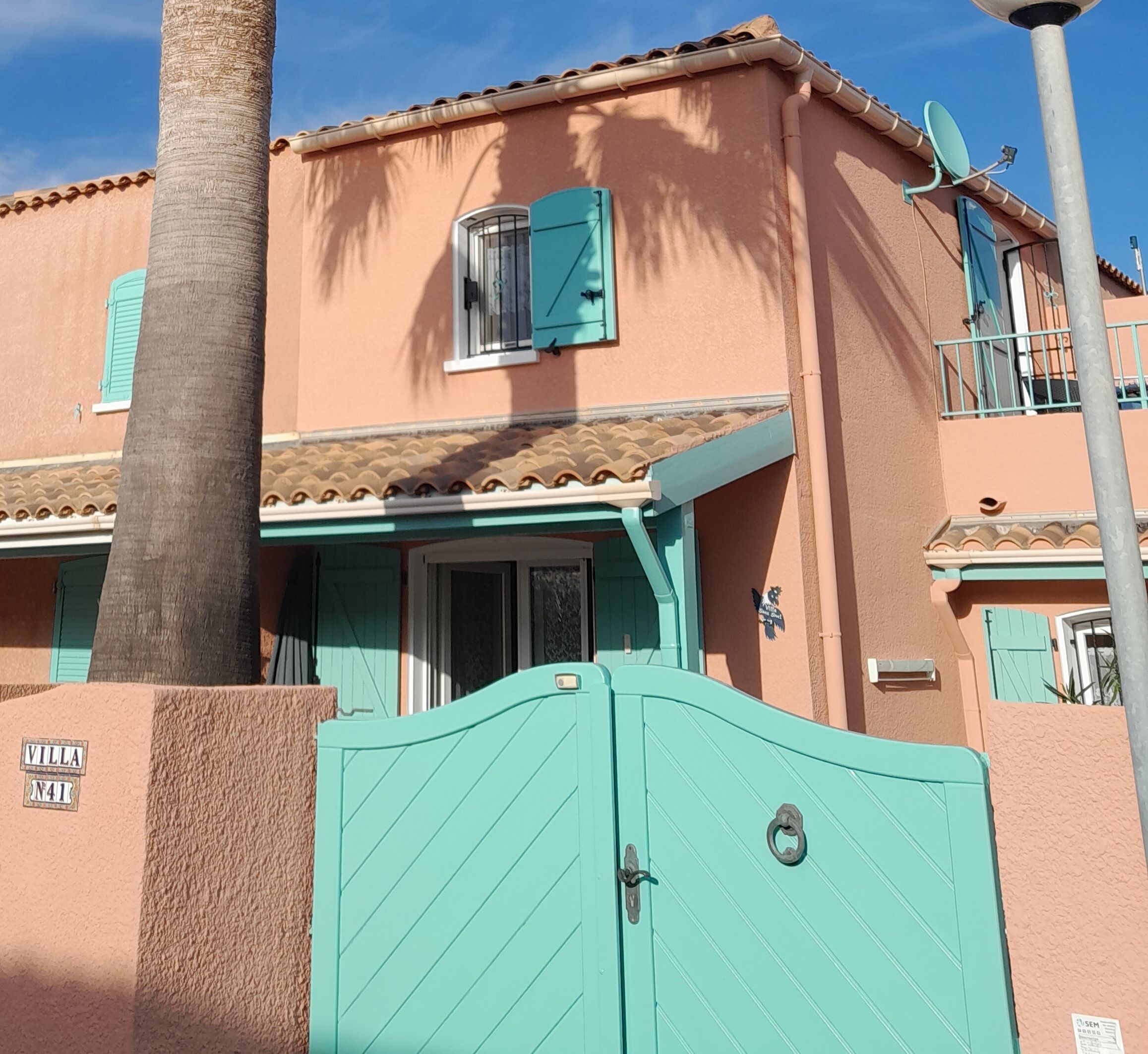 Un immeuble doté d’une porte turquoise, d’un balcon et d’une antenne parabolique.