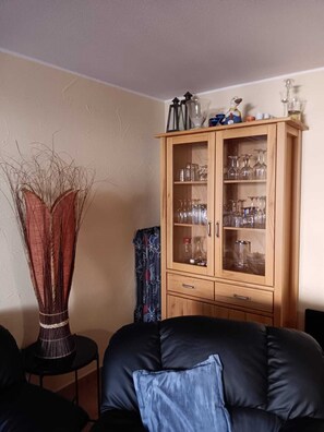 Een woonkamer met een donker leren bank, een houten kast met glazen deuren en een decoratieve vaas.