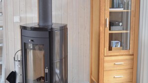 Una sala de estar moderna con un estufa de leña negra, un mueble de madera con puertas de vidrio y una gran pintura de Buda en la pared.
