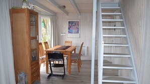 Un comedor con mesa y sillas de madera, un armario con puertas de cristal y una escalera en espiral blanca.