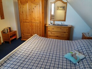 Une chambre avec une couvre-lit à carreaux, une armoire en bois, une commode et un miroir au mur.