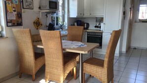 Une cuisine avec des meubles blancs, un four à micro-ondes et une table à manger entourée de chaises en osier.