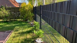 Une clôture métallique moderne dans un jardin bien entretenu, avec de la pelouse et de petites plantes.