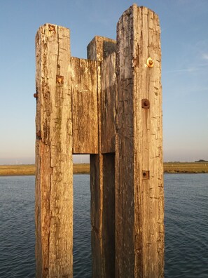 Une structure en bois usée par les intempéries, avec des boulons rouillés, se dressant sur fond d’une étendue d’eau calme et d’éoliennes éloignées.