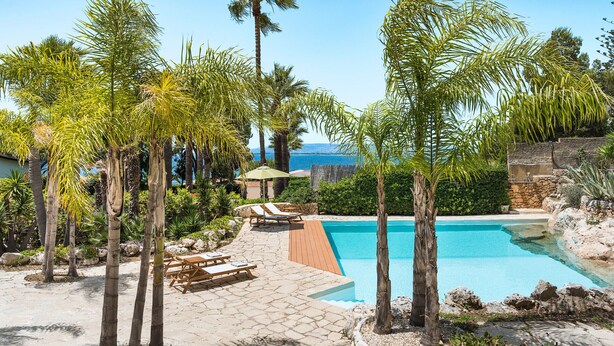 Zona de piscina con palmeras, sillas de descanso y vistas al mar.