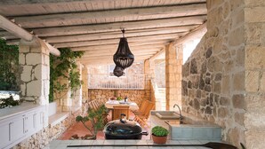 Cocina con paredes de piedra, techo de madera, lámpara colgante, una mesa de comedor con sillas y una planta en maceta.