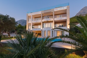 Um hotel com vários andares, piscina, rodeado por vegetação e montanhas.