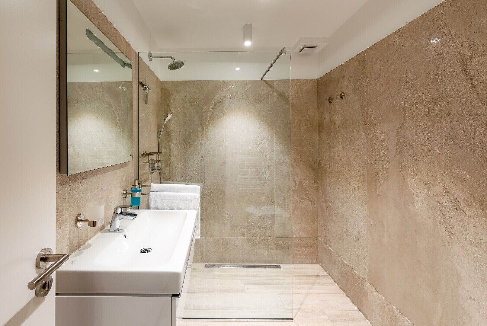 A modern bathroom with two sinks, a large mirror, and a walk-in shower.