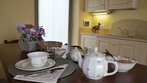 A dining table set with white teacups, saucers, a teapot, and a bowl of cereal. There is a vase with flowers on the table, and a basket of bread. - LA CASINA DEL BIONDO - LA CASINA DEL BIONDO (Monte San Savino)
