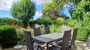 A patio with a table and chairs, surrounded by greenery and a swing set. - Large, cozy vacation home with garden between St. Peter-Ording & Büsum (Wesselburen)