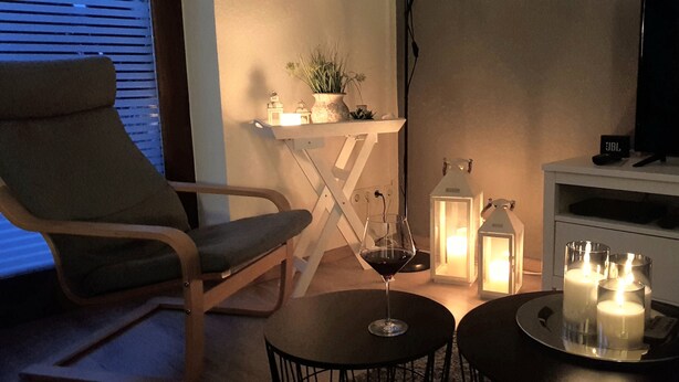 A cozy living room with a wooden armchair, a small round table with a wine glass, candles, and a TV on a stand. - Large, cozy vacation home with garden between St. Peter-Ording & Büsum (Wesselburen)